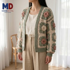 May include: A long-sleeved crochet cardigan featuring a granny square pattern with sage green and cream borders and raised, textured floral centers in dusty rose. The open-front garment has a ribbed sage green trim along the neckline and cuffs.
