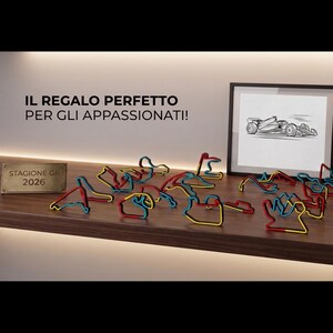 Può includere: Un'esposizione di modelli di circuiti di gara a filo colorati in rosso, blu e giallo, disposti su una mensola di legno. Sono presenti anche uno schizzo incorniciato di un'auto da corsa e del testo in italiano.