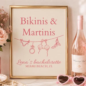 Może przedstawiać: Prostokątny znak w złotej ramie z kremowym tłem i różowym napisem Bikinis & Martinis, Lena's bachelorette oraz MIAMI BEACH, FL. Znak zawiera różowy rysunek liniowy przedstawiający bikini, pierścionek i buty na wysokim obcasie.