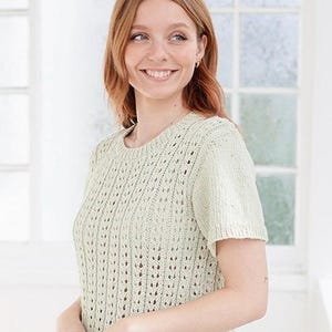 Puede incluir: Una blusa de punto de manga corta en color verde salvia claro con un patrón de calados verticales, cuello redondo y dobladillo acanalado. La prenda está confeccionada con un tejido de punto texturizado y transpirable con un efecto rayado.