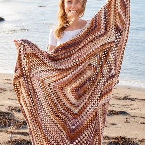 Puede incluir: Una manta de ganchillo cuadrada y grande con un patrón clásico de granny square. El diseño muestra filas concéntricas de hilo en tonos tierra, incluyendo matices de crema, beige, rosa empolvado, terracota y marrón oscuro, creando una paleta cálida.
