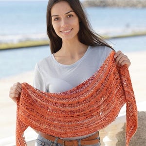 Puede incluir: Un chal triangular tejido a mano en tonos vibrantes de naranja, óxido y cobre. El accesorio presenta un patrón de encaje abierto y aireado con rayas horizontales texturizadas y extremos largos y cónicos que caen a ambos lados.