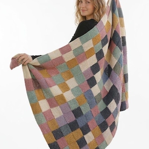 Puede incluir: Una manta de punto multicolor con un patrón de tablero de ajedrez. La manta presenta cuadrados de varios colores, incluyendo rosa, azul, verde, beige y gris. La manta se sostiene, mostrando su textura y diseño.