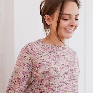 Puede incluir: Un suéter de punto de manga corta con un patrón de hilo jaspeado multicolor en tonos dominantes de rosa suave, lavanda y sutiles motas de verde y amarillo. La prenda presenta un cuello redondo y mangas raglán con bordes acanalados.