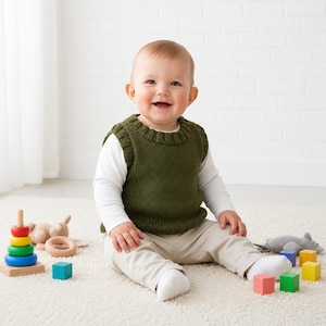 Puede incluir: Un bebé sonriente con un chaleco verde tejido sobre una camiseta blanca de manga larga y pantalones color caqui. El bebé está rodeado de juguetes de madera coloridos, incluyendo un juguete de anillos apilables, bloques y un ratón de peluche.