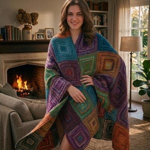 Puede incluir: Un chal colorido con un patrón geométrico en tonos turquesa, morado, verde y naranja. El chal está drapeado sobre una persona, mostrando el intrincado diseño de punto. El fondo incluye una chimenea, libros y una lámpara.