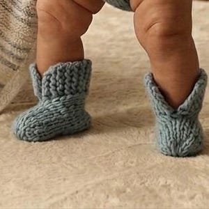 Puede incluir: Un par de botines de bebé de punto azul claro. Los botines tienen un puño doblado y un estilo de bota de vaquero. La lana suave y texturizada crea un aspecto acogedor y cómodo. Los botines están diseñados para bebés.