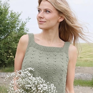 Puede incluir: Una camiseta de punto sin mangas en color verde salvia con escote cuadrado, tirantes anchos y un patrón texturizado de pequeños detalles de ojales en la parte delantera. La prenda tiene un borde de punto acanalado en el cuello y el dobladillo.
