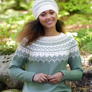 Puede incluir: Un suéter de punto en color verde salvia y crema con un canesú circular que presenta un patrón geométrico de diamantes y un gorro de punto a juego con un diseño similar, ambos con cuello, puños y dobladillo acanalados de textura suave.