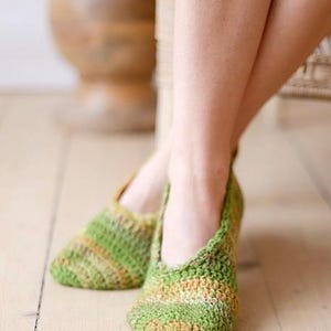 Puede incluir: Un par de zapatillas bajas confeccionadas con hilo jaspeado en tonos verde, amarillo y naranja. Las zapatillas presentan un patrón de punto de ganchillo texturizado con puntera redondeada y un diseño sencillo sin cordones que cubre el pie.