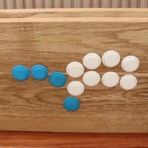 May include: A wooden arcade controller with a light brown finish. It has a layout of blue and white buttons. The buttons are arranged in a classic arcade configuration, suitable for gaming.