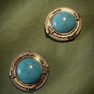 May include: Two round buttons featuring a central turquoise stone with dark veining, encased in a gold-toned metal frame with a rope-like border and decorative accents. The text "Bohemian Turquoise" is printed in the upper left corner.