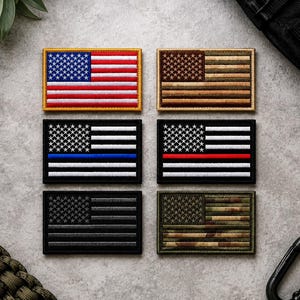 May include: Six rectangular embroidered patches featuring the United States flag in various color schemes. The top left is red, white, and blue. The top right is tan and brown. The middle left is black and white with a blue stripe. The middle right is black and white with a red stripe. The bottom left is black and grey. The bottom right is green and brown camouflage.