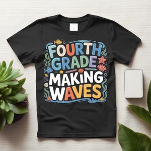 May include: A black short-sleeve t-shirt featuring a colorful graphic with the text "FOURTH GRADE MAKING WAVES". The design includes illustrations of fish, a starfish, seashells, seaweed, and pencils in shades of blue, orange, and yellow.