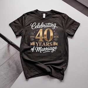 Può includere: Una t-shirt nera a maniche corte con testo e grafica color oro. Il design mostra le parole Celebrating 40 YEARS of Marriage, con gli anni 1986 e 2026 su entrambi i lati del grande numero 40, accentuato da piccole icone a forma di stella.