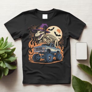 Peut inclure: Un t-shirt noir à manches courtes avec une impression graphique représentant un squelette de Tyrannosaure Rex portant un chapeau de sorcière violet, debout sur un monster truck bleu. Le fond inclut une grande lune orange, des chauves-souris, des toiles d'araignée et des flammes.