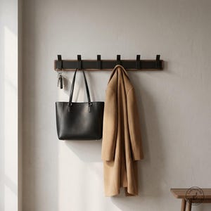 Peut inclure: Un porte-manteau mural composé d'une base en bois foncé avec six crochets en métal noir. Un sac fourre-tout en cuir noir est suspendu à un crochet, un trousseau de clés à un autre, et un manteau en laine beige est accroché au troisième crochet.