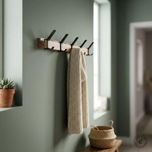 May include: A wall-mounted coat rack featuring a natural light-colored wooden base with five matte black metal hooks. A thick, cream-colored knitted scarf hangs from one of the hooks, draping downwards in a vertical orientation.