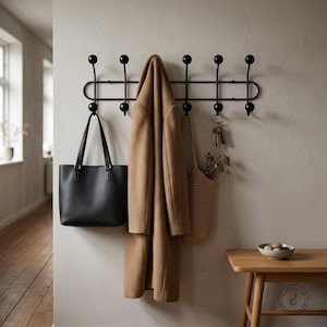 Peut inclure: Un porte-manteau mural en métal noir doté de dix crochets arrondis disposés sur deux rangées horizontales. Un manteau en laine beige, un sac fourre-tout en cuir noir, un sac tissé beige et un trousseau de clés sont suspendus aux crochets.