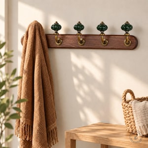 May include: A wall-mounted coat rack featuring a horizontal dark wood base with four brass hooks, each topped with a round, ribbed, dark green ceramic knob. A textured brown towel hangs from the leftmost hook of the rack.