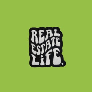May include: An embroidered patch featuring the text "REAL ESTATE LIFE" in white, with a black border. The patch has a retro font and is set against a bright green background.