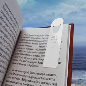 May include: A white, rectangular bookmark with rounded edges and a cutout at the top, featuring the text MISTY FLOW and a small botanical illustration, placed inside an open book with printed Latin text against a blurred ocean background.