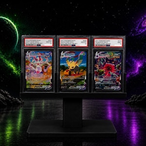 Puede incluir: Tres cartas coleccionables graduadas exhibidas en un soporte negro. Las cartas son Pokemon SWSH 2021 Sylveon VMAX, Leafeon VMAX y Gengar VMAX, cada una encapsulada en una funda protectora de plástico con una etiqueta blanca con la calificación.