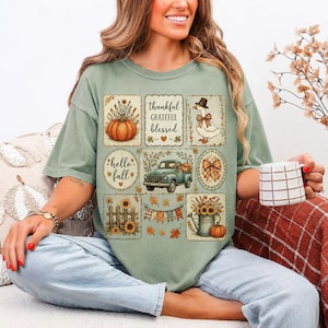 May include: A sage green t-shirt featuring a grid of nine illustrations including a pumpkin, a duck with a bow, a vintage truck, a watering can, sunflowers, and a banner. The text reads thankful, grateful, blessed, and hello fall.