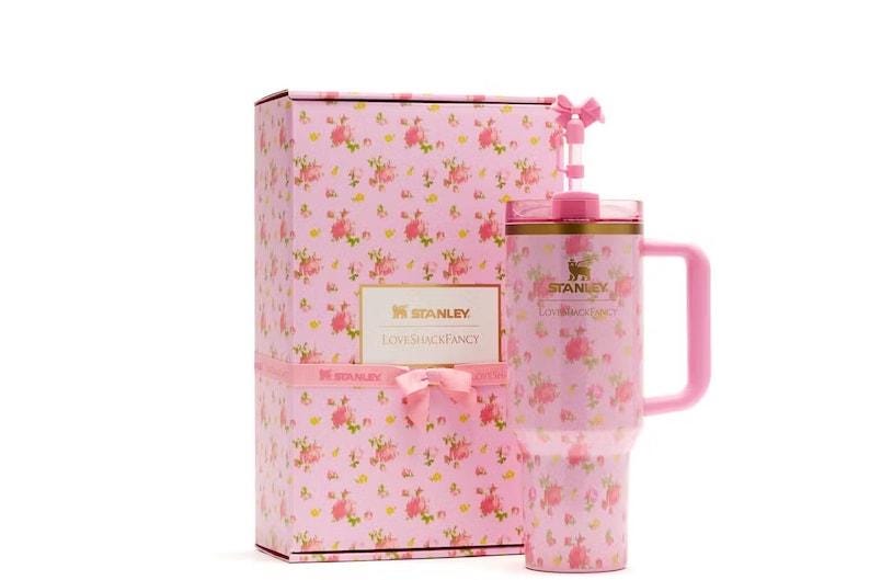 Op de afbeelding: Een roze Stanley LoveShackFancy-beker met een bloemenpatroon, een bijpassend handvat en een rietje met een kleine roze strik. De beker staat naast een rechthoekige geschenkdoos met hetzelfde roze bloemendesign en de merknaam erop.