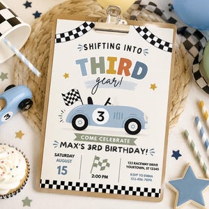 May include: A rectangular birthday invitation on a wooden clipboard featuring a light blue race car with the number 3, a checkered flag, and the text Shifting into Third Gear! Come Celebrate Max's 3rd Birthday! Saturday August 15 2:00 PM.