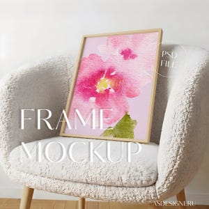Op de afbeelding: Een lichthouten lijst met een aquarel-stijl print van roze bloemen met een geel hart en een groen blad op een lichtroze achtergrond. De tekst PSD FILE is rechtsboven zichtbaar en FRAME MOCKUP staat in het midden van de afbeelding.