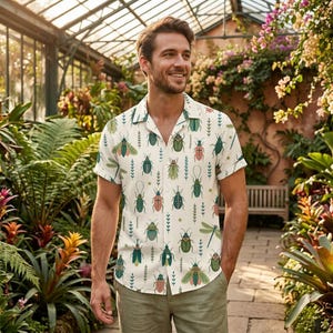 May include: A short-sleeved button-down shirt in an off-white color featuring a repeating pattern of various insects including beetles and dragonflies in shades of green, pink, and brown, paired with plain light olive green trousers.