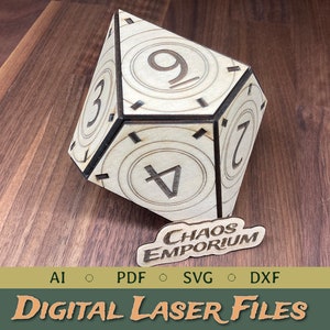 Puede incluir: Un dado de madera de seis caras, cortado con láser, con los números del 1 al 6 en cada cara. El dado tiene forma de cubo y está apoyado sobre una superficie de madera. El dado está etiquetado como "Chaos Emporium".