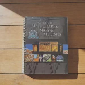 May include: A spiral-bound book titled "Rose Book of Bible Charts, Maps & Time Lines." The cover features images of biblical scenes and a 10th Anniversary seal. The book is wrapped in clear plastic and rests on a wooden surface.