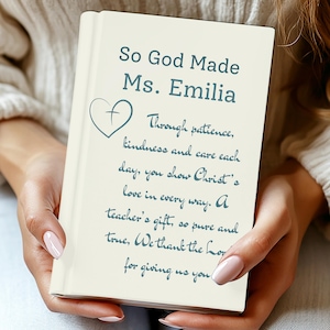 Puede incluir: Un libro color crema con el texto "So God Made Ms. Emilia" y una cruz en forma de corazón. El libro contiene un poema sobre el regalo de un profesor. El libro está sostenido por una persona.