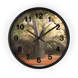 May include: A round wall clock with a black frame and a printed face featuring an oil painting of a large tree with spreading branches. The clock has black hour, minute, and second hands, and large black Arabic numerals from one to twelve.