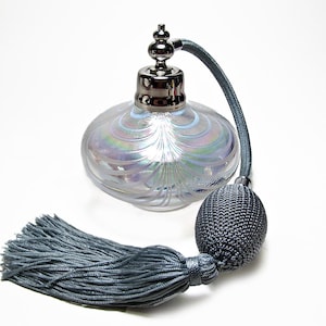 May include: A vintage-style perfume bottle made of iridescent glass, featuring a silver-toned metal top and a matching blue atomizer and tassel. The bottle has a round shape with a decorative swirl pattern. The tassel is a muted blue.