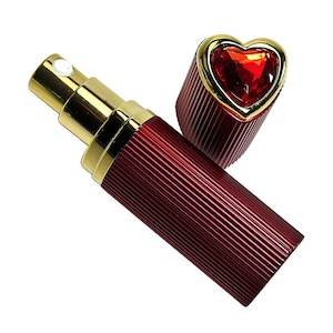 Puede incluir: Un atomizador de perfume rojo y dorado con una tapa en forma de corazón. El atomizador tiene un diseño acanalado y una boquilla rociadora dorada. La tapa en forma de corazón es dorada y presenta una gema roja.