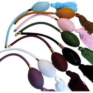 May include: A collection of vintage-style perfume atomizers in various colors, including blue, pink, green, and black. Each atomizer has a bulbous body, a curved tube, and a tassel. The metal accents are gold-toned.
