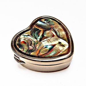 May include: A heart-shaped metal trinket box with a polished silver-tone finish. The lid features an inlay of iridescent abalone shell pieces, displaying a variety of shimmering green, blue, and purple tones across the surface of the container.