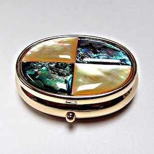 May include: An oval-shaped gold-toned metal compact case featuring a decorative inlay on the lid. The inlay is divided into four quadrants, alternating between iridescent abalone shell with green and blue tones and smooth cream-coloured mother-of-pearl.