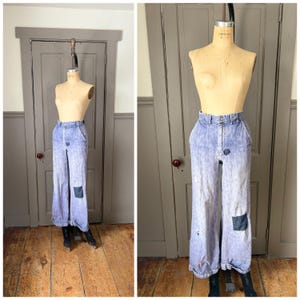 May include: Acid wash denim pants with a high waist and wide legs. The light blue jeans feature a button closure, pockets, and dark blue patches on the knees. The pants are displayed on a mannequin.