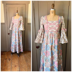 May include: A vintage floral print maxi dress with a square neckline and bell sleeves. The dress features a patchwork design in shades of pink, blue, and cream. The dress is displayed on a mannequin.