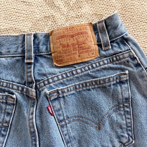 May include: Close-up of light blue denim jeans with a brown leather label. The label reads "LEVI STRAUSS & CO. ORIGINAL RIVETED QUALITY CLOTHING" and "550". The jeans have a red Levi's tag on the back pocket.