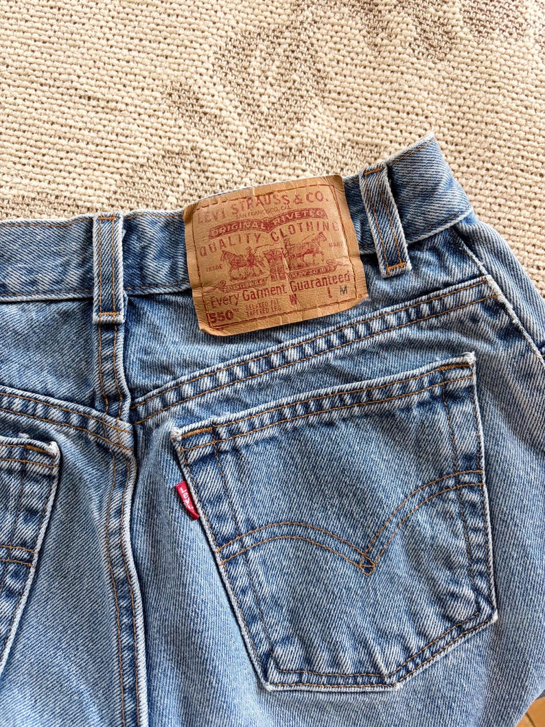 May include: Close-up of light blue denim jeans with a brown leather label. The label reads "LEVI STRAUSS & CO. ORIGINAL RIVETED QUALITY CLOTHING" and "550". The jeans have a red Levi's tag on the back pocket.