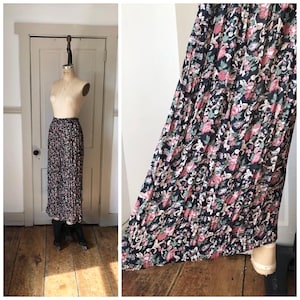 May include: A black and pink floral print maxi skirt with pleats. The skirt is made of a lightweight fabric and has a flowy silhouette.