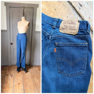 Könnte beinhalten: Blaue Jeans aus Denim an einer Schaufensterpuppe. Die Jeans haben eine klassische Passform mit geradem Bein und eine hohe Taille. Die Gesäßtasche zeigt das Logo von Levi Strauss & Co. Die Jeans werden auf einem Holzboden präsentiert.