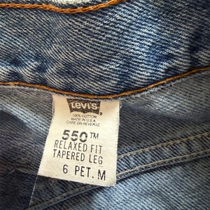 May include: Close-up of a pair of blue denim jeans. The Levi's tag is visible, displaying "550 Relaxed Fit Tapered Leg" and size "6 PET. M". The jeans are made of 100% cotton and made in the USA.