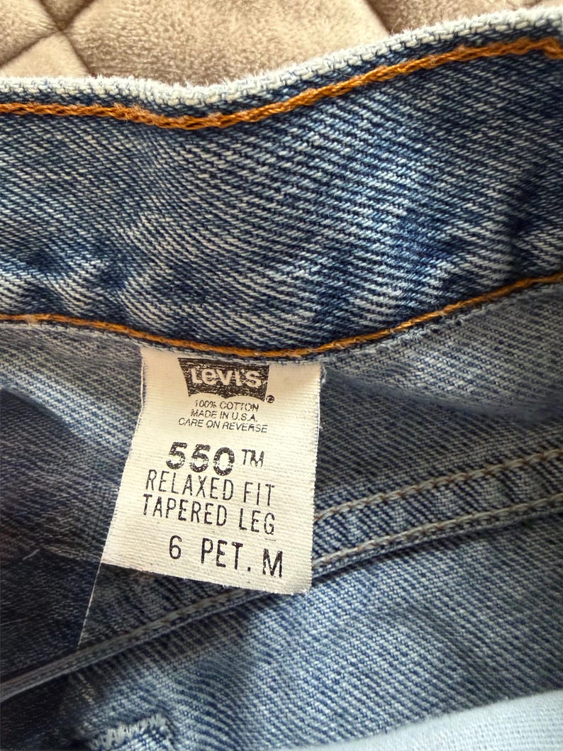 May include: Close-up of a pair of blue denim jeans. The Levi's tag is visible, displaying "550 Relaxed Fit Tapered Leg" and size "6 PET. M". The jeans are made of 100% cotton and made in the USA.