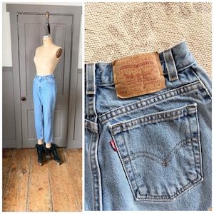May include: Light blue denim jeans displayed on a mannequin. The jeans have a classic fit and are cuffed at the ankles. A close-up shows the back pocket with a red Levi's tag and a brown leather label.